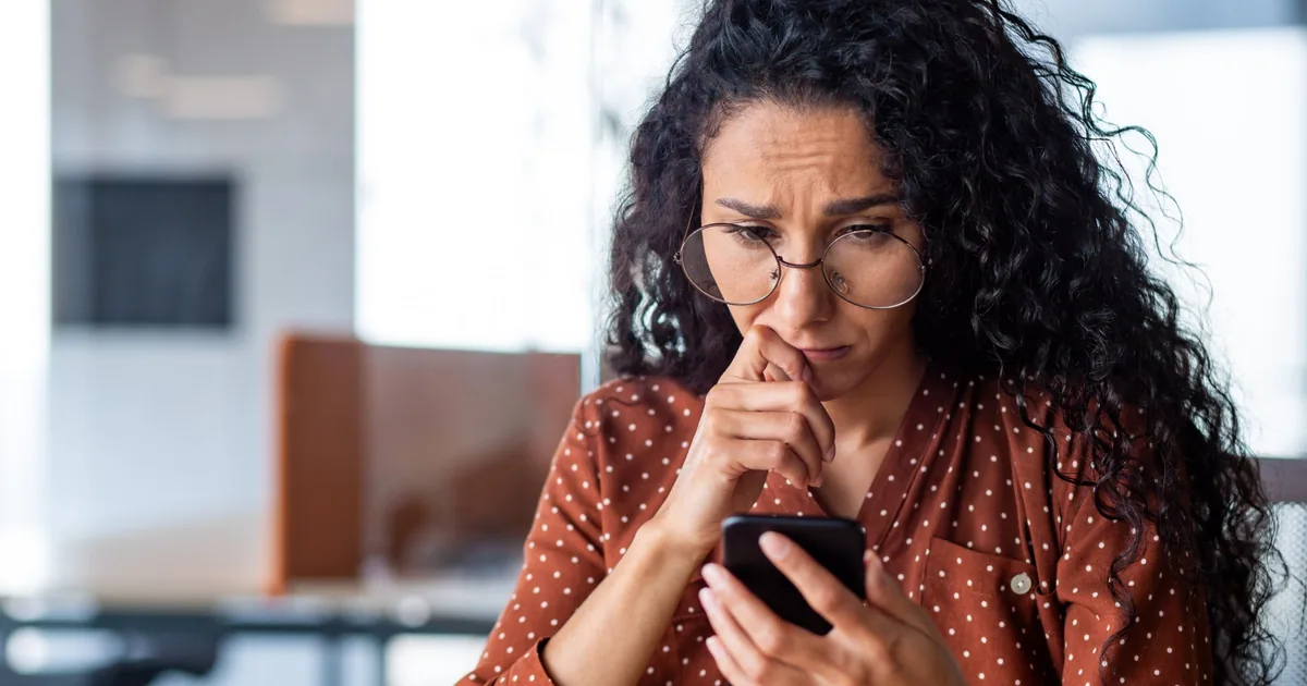 Frau mittleren Alters schaut nachdenklich auf ihr Smartphone