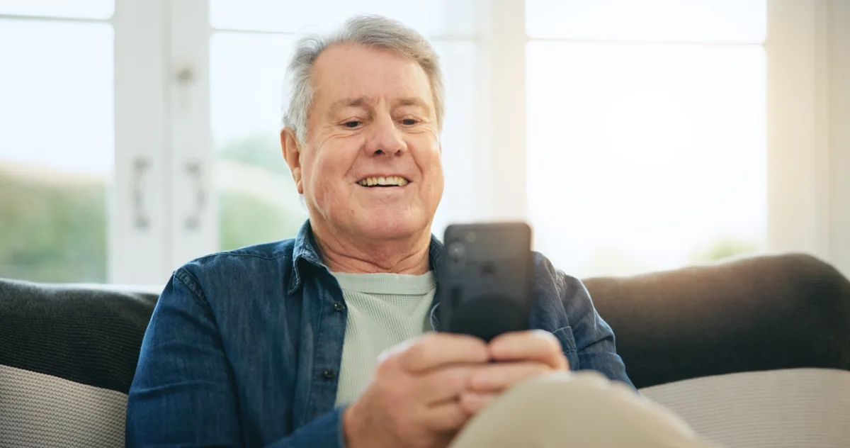 Älterer Mann auf dem Sofa, entspannt mit Smartphone lächelnd